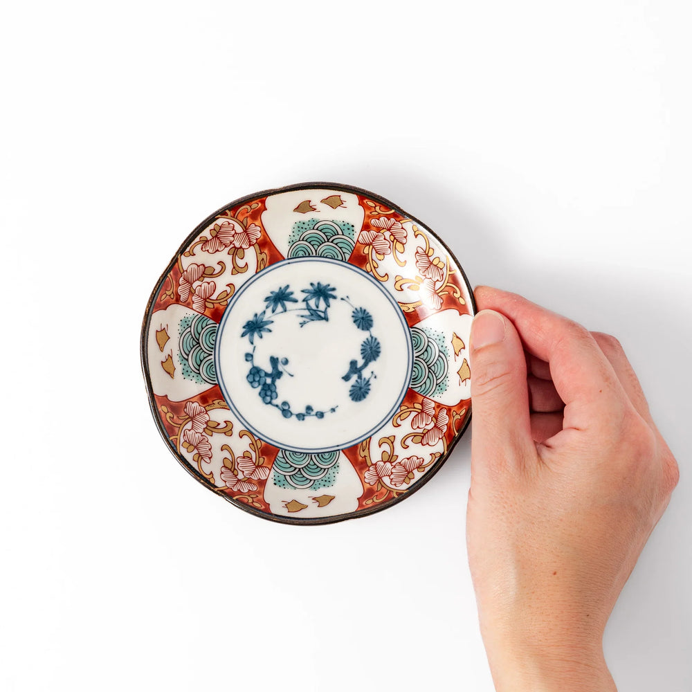 Scalloped sauce dish with red blue and green Japanese motifs and floral center for elegant dining.