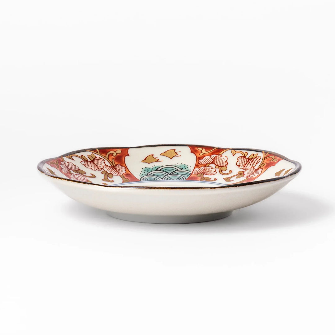 Scalloped sauce dish with red blue and green Japanese motifs and floral center for elegant dining.