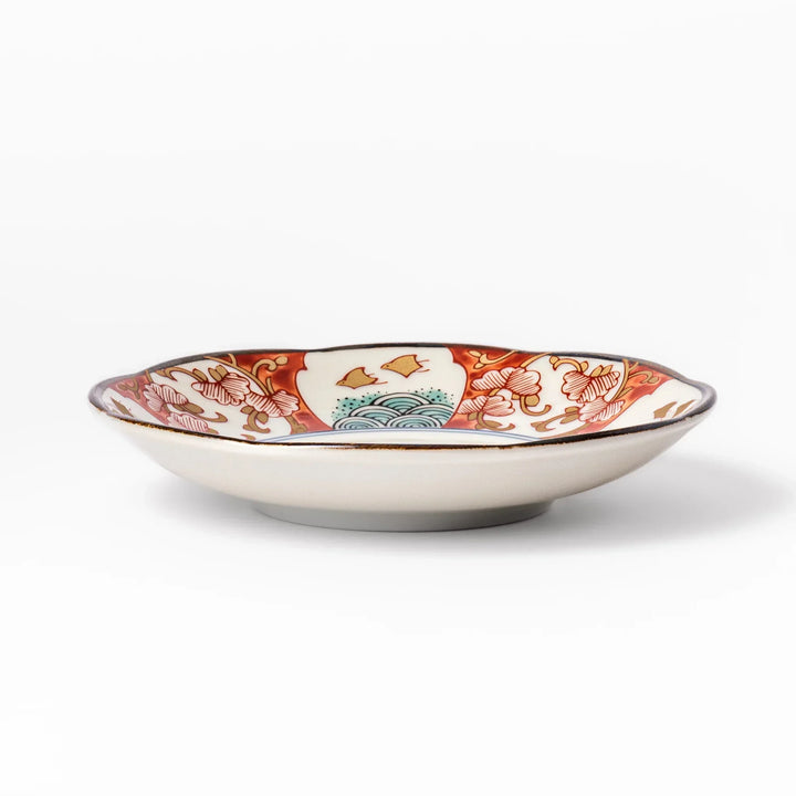 Scalloped sauce dish with red blue and green Japanese motifs and floral center for elegant dining.