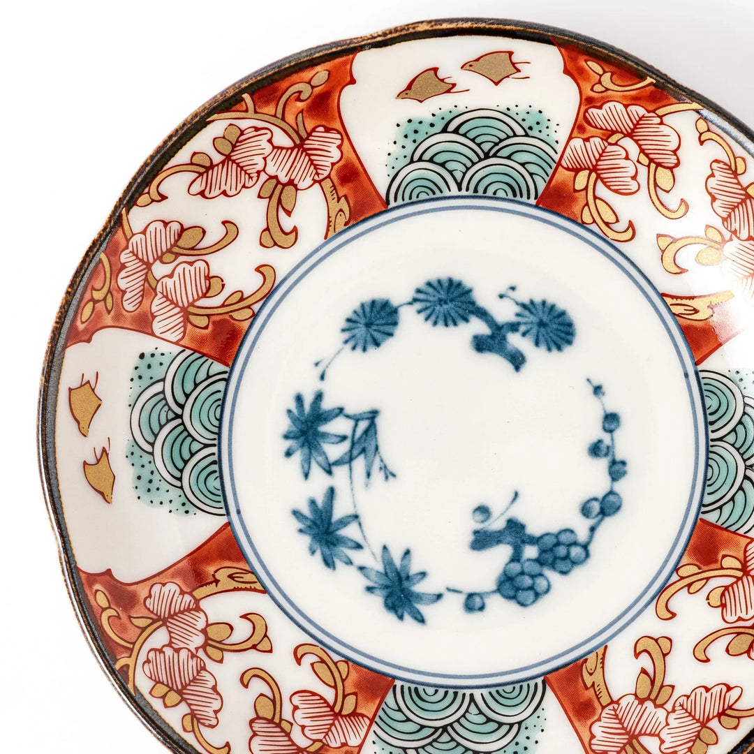 Scalloped sauce dish with red blue and green Japanese motifs and floral center for elegant dining.