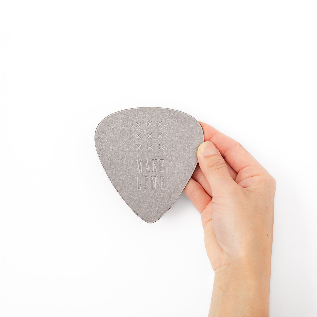 Unique guitar pick shaped metal coaster with sandblasted textured finish engraved with make line text and cross patterns