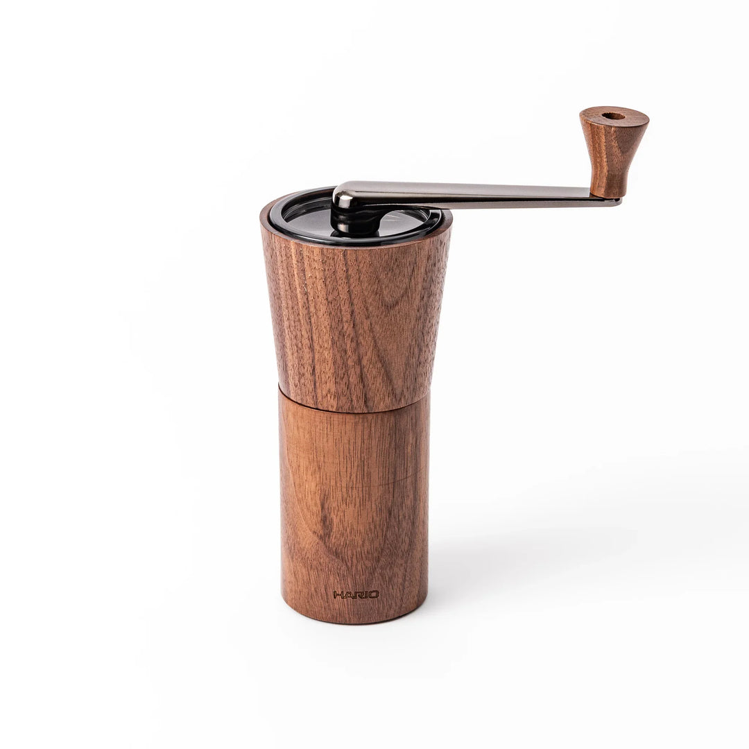 HARIO walnut wood manual coffee grinder with a hand crank, featuring a sleek natural wooden body on a white background