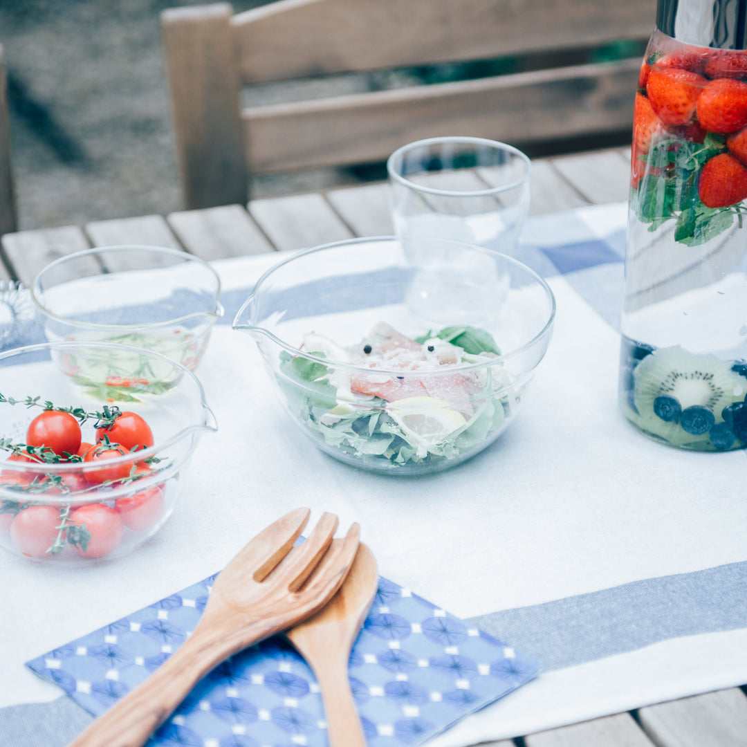 Hario heatproof glass mixing bowls with fresh salad and fruit infused water pitcher on wooden outdoor dining table