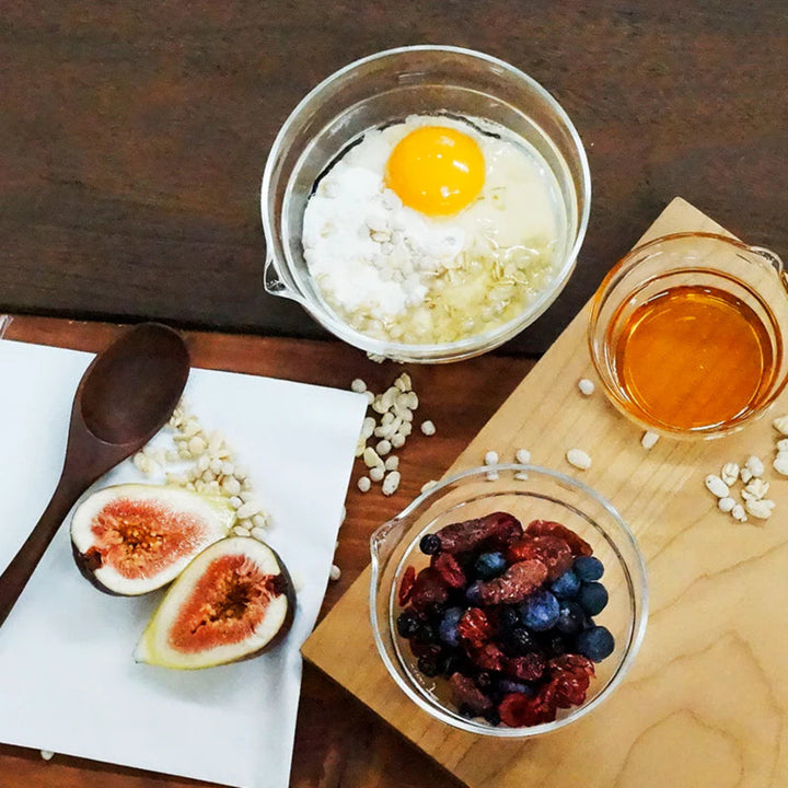 Mixing egg yolk and oatmeal in hario heatproof glass lip bowl near fresh figs dried berries and honey breakfast