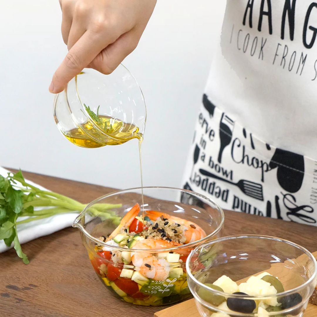 Pouring olive oil from a small hario glass lip bowl into a large mixing bowl with shrimp salad cooking preparation