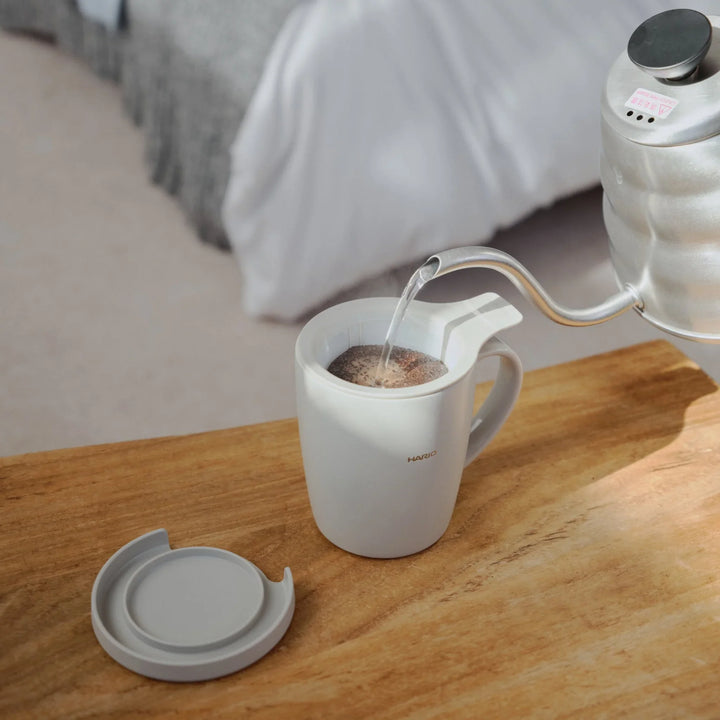 Resting mesh infuser filter on top of hario ceramic tea and coffee mug on a wooden bedroom table near books