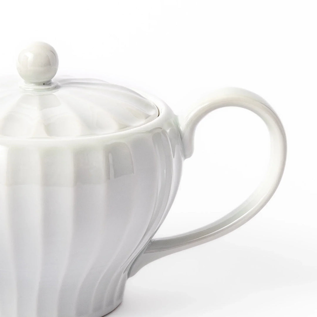 White teapot with vertical petal-inspired ridges and a round lid, perfect for a refined and elegant tea presentation.