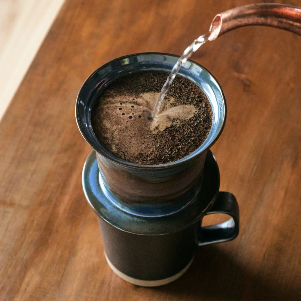 Handcrafted ceramic coffee dripper in use with hot water pouring over fresh grounds for rich single serve pour over brewing.