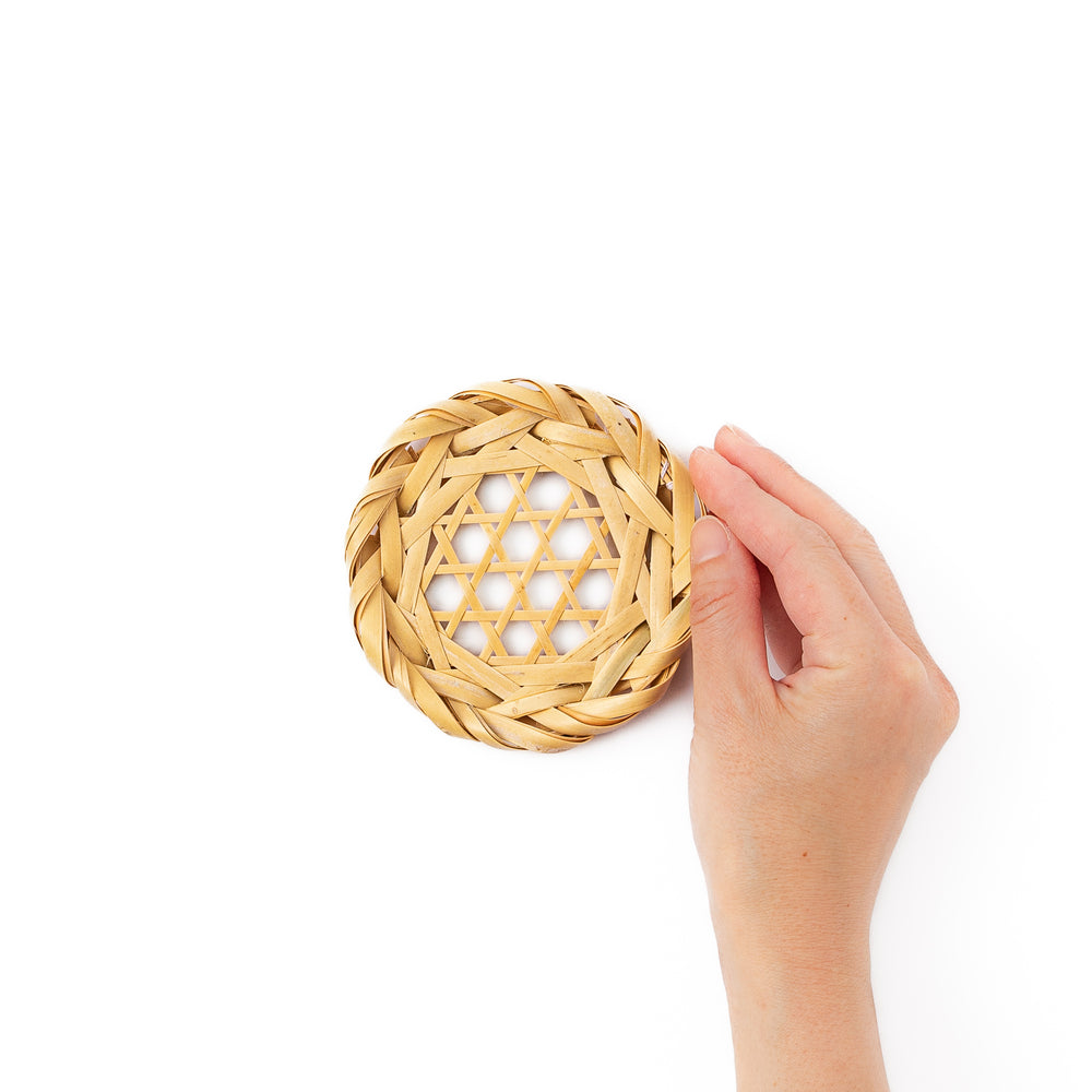 A round handwoven bamboo drink coaster showcasing a traditional star pattern weave and a braided natural fiber border