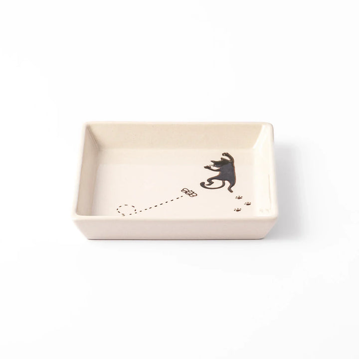 Square beige plate featuring a playful black cat chasing a butterfly, with paw prints and a dotted flight path.