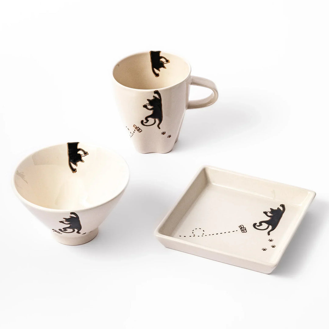 Matching mug, bowl, and square plate set in beige with playful black cat and butterfly designs.