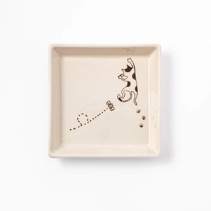 Beige square plate with playful calico cat and butterfly illustration, accented with dotted lines and paw prints.