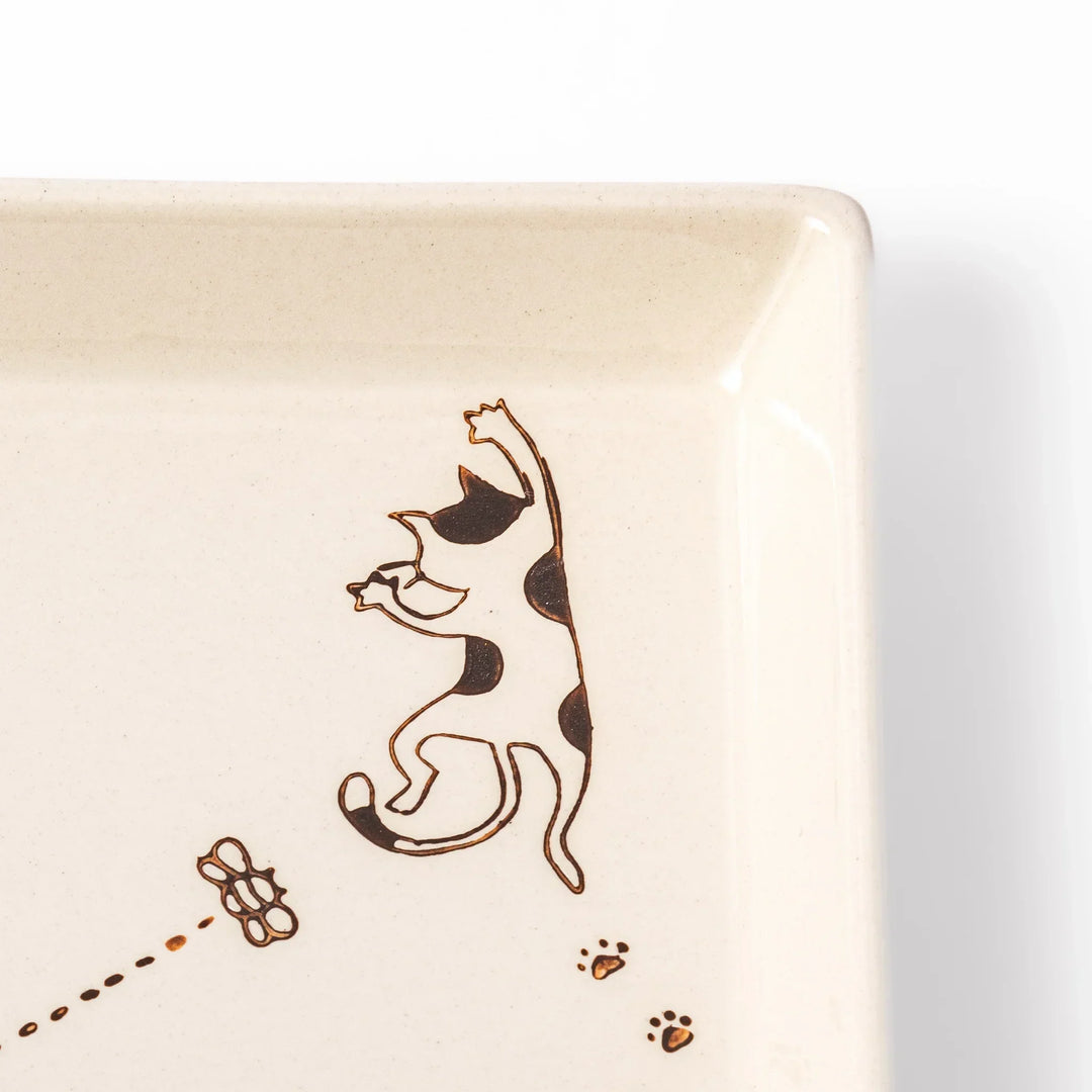Beige square plate with playful calico cat and butterfly illustration, accented with dotted lines and paw prints.