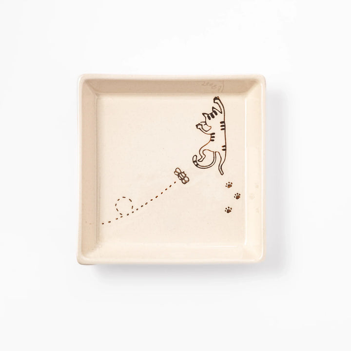 Beige square plate featuring a tabby cat chasing a butterfly with dotted trail and small paw prints.