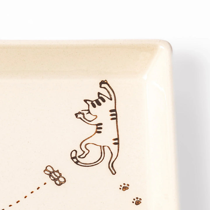 Beige square plate featuring a tabby cat chasing a butterfly with dotted trail and small paw prints.