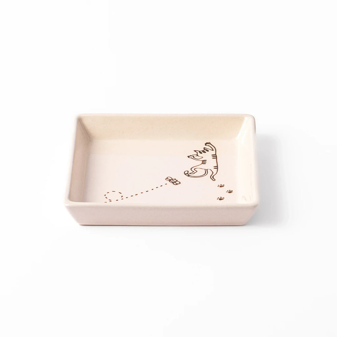 Beige square plate featuring a tabby cat chasing a butterfly with dotted trail and small paw prints.