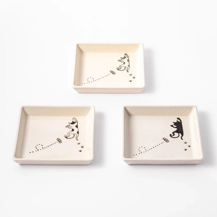 Three square plates with playful cat designs showing a tabby, calico, and black cat chasing a butterfly with paw prints.