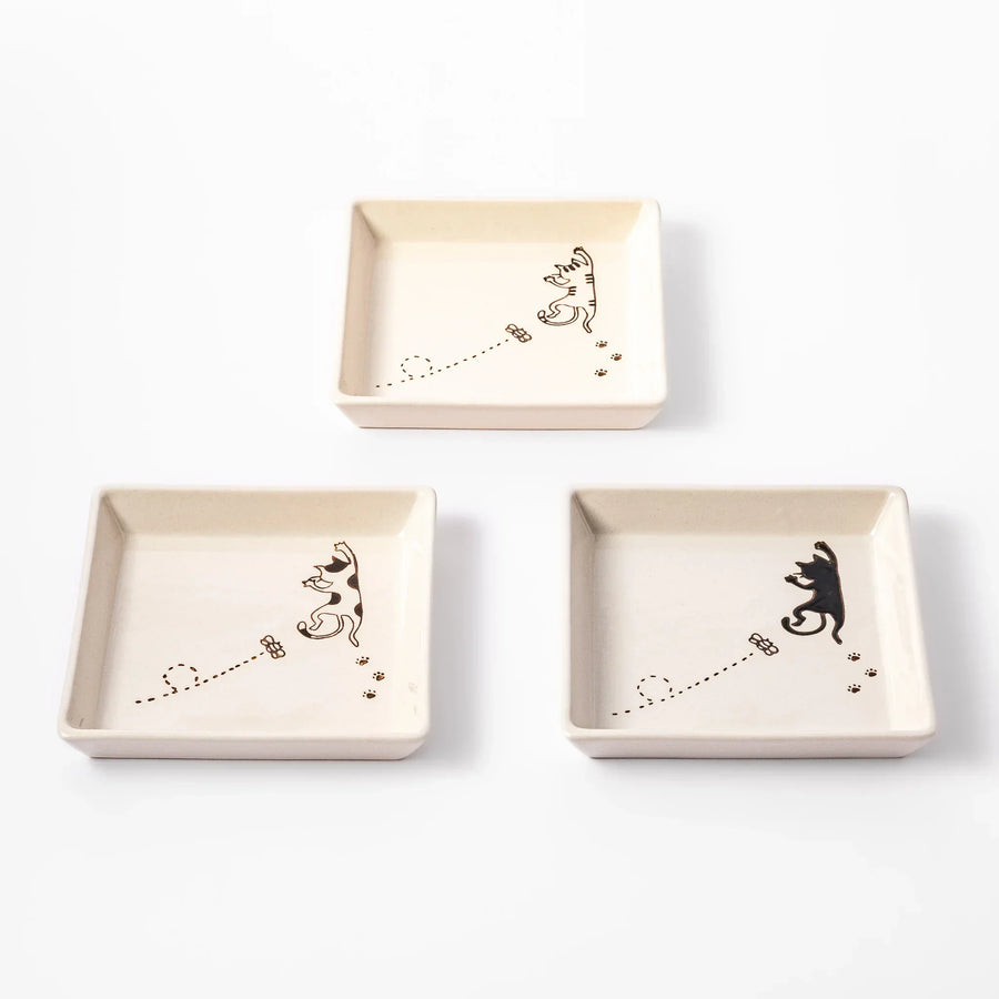 Three square plates with playful cat designs showing a tabby, calico, and black cat chasing a butterfly with paw prints.