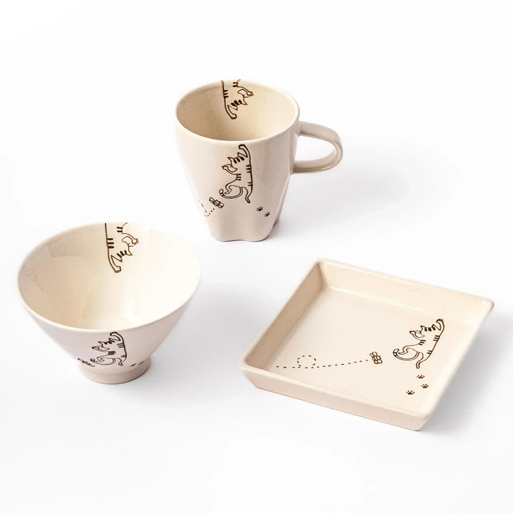 Matching mug, bowl, and square plate featuring a striped cat chasing a butterfly with dotted lines and paw prints.