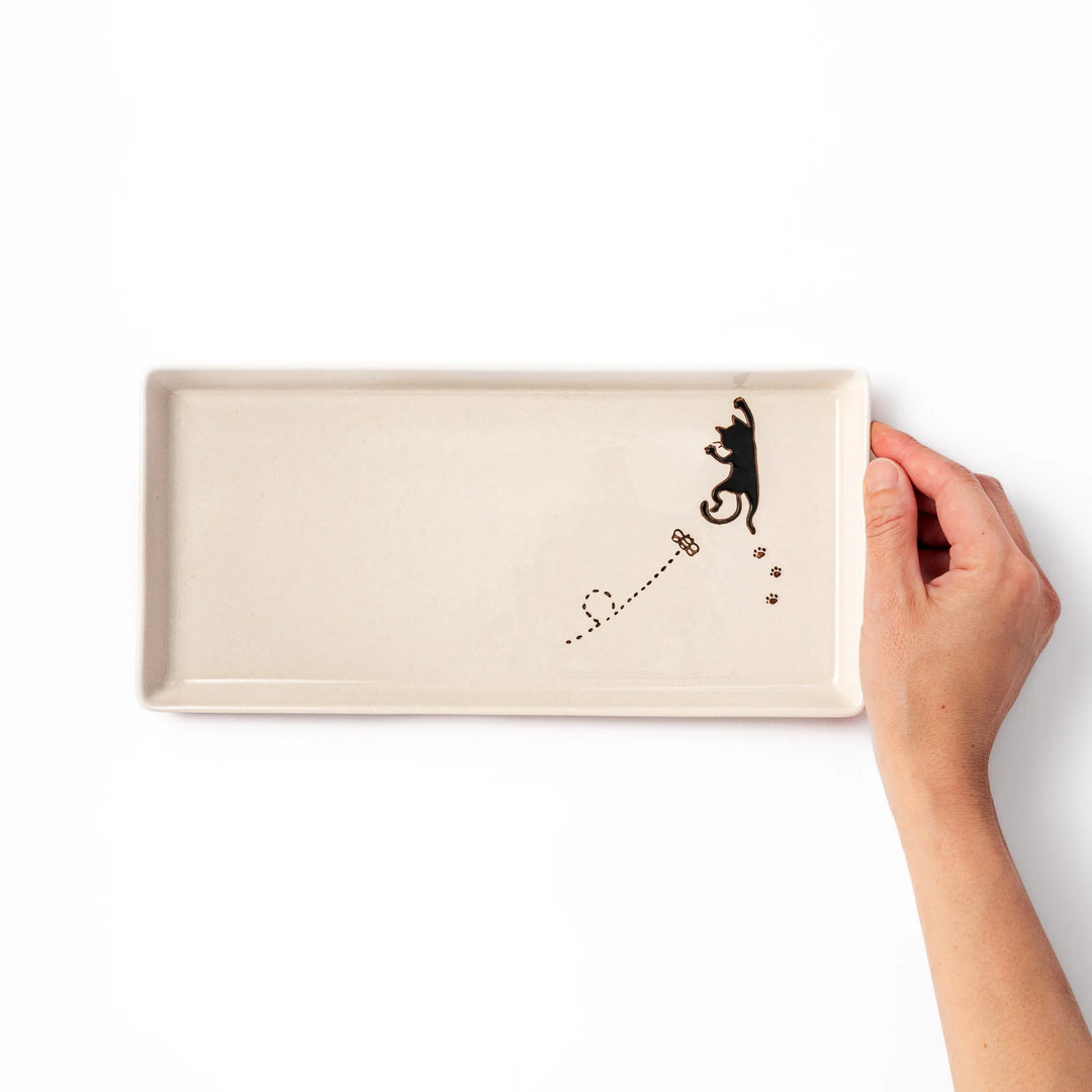 Beige rectangular ceramic plate featuring a playful black cat illustration with paw prints and a butterfly in the corner.