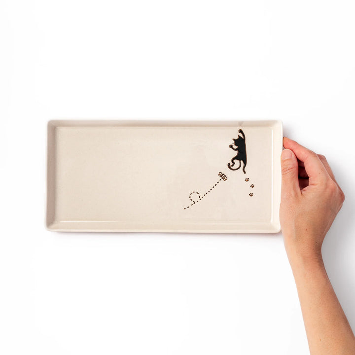 Beige rectangular ceramic plate featuring a playful black cat illustration with paw prints and a butterfly in the corner.