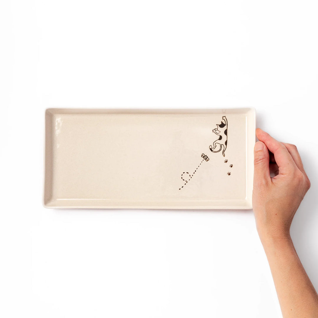 Beige rectangular ceramic plate featuring a playful calico cat illustration with paw prints and a butterfly in the corner.