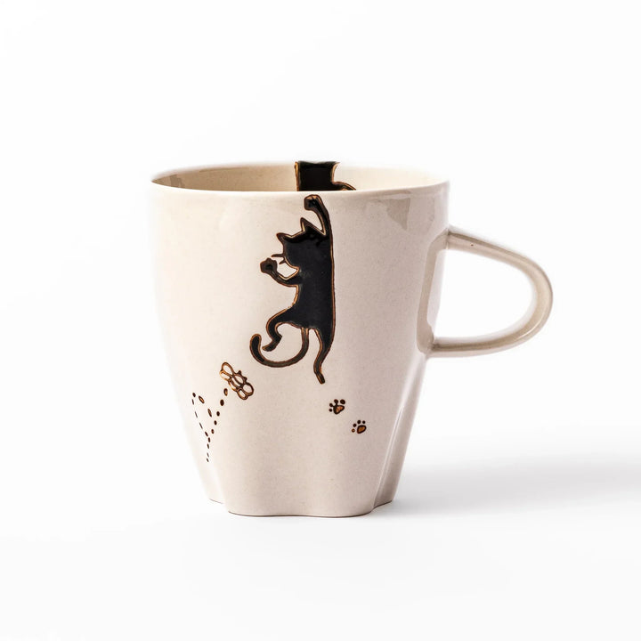 Cream-colored cup with a black cat design reaching for a butterfly, accented by playful dotted lines and paw prints.