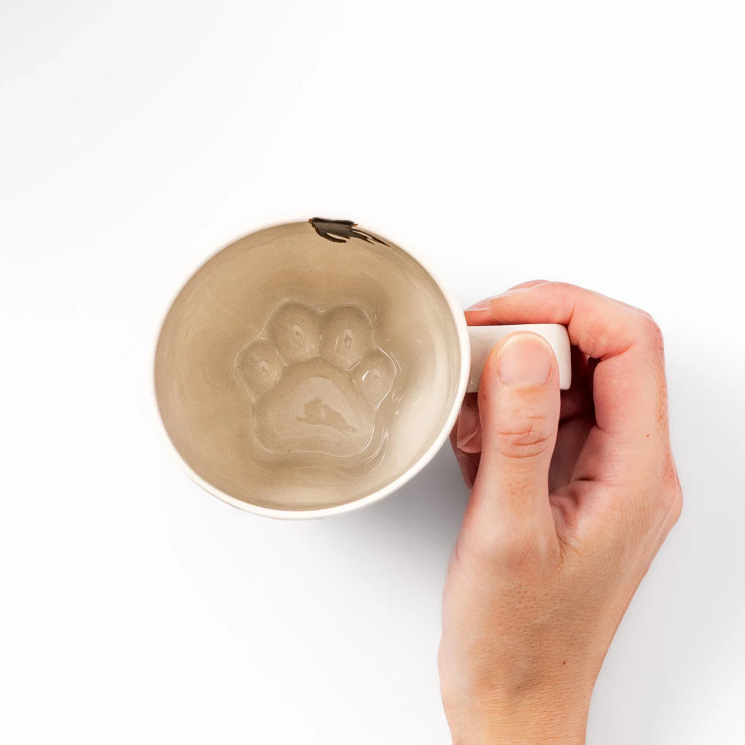 Cream-colored cup with a black cat design reaching for a butterfly, accented by playful dotted lines and paw prints.