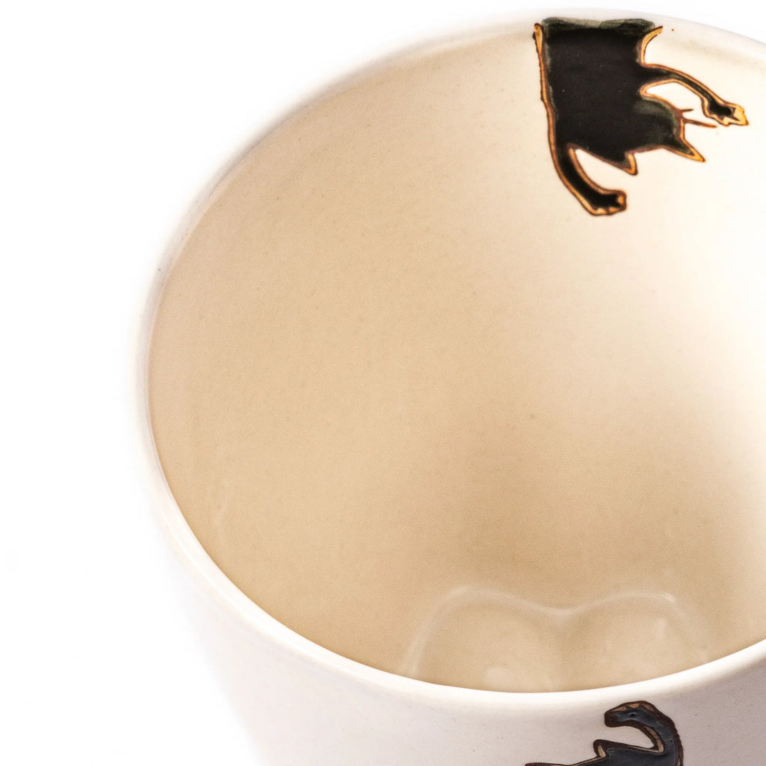 Cream-colored cup with a black cat design reaching for a butterfly, accented by playful dotted lines and paw prints.