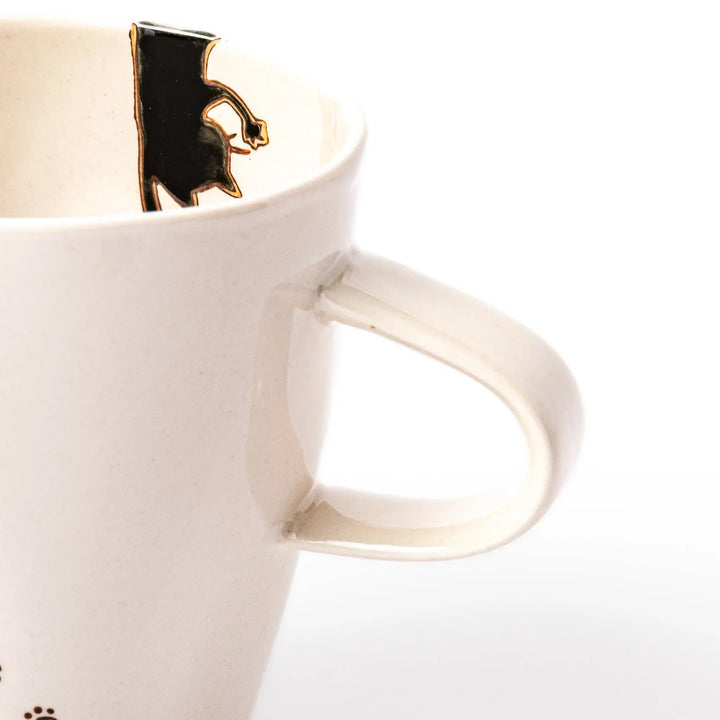 Cream-colored cup with a black cat design reaching for a butterfly, accented by playful dotted lines and paw prints.