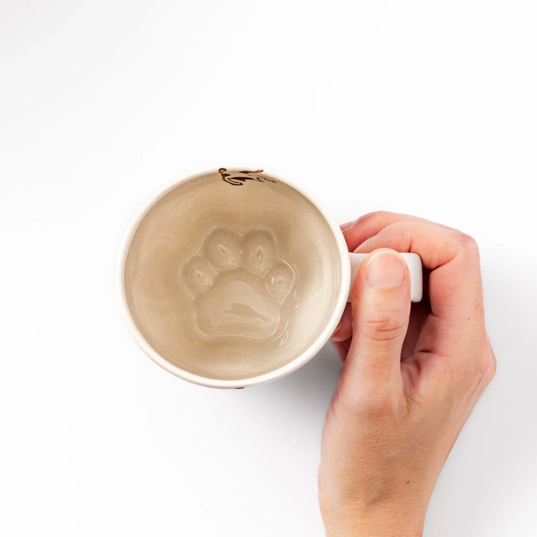 Cream-colored cup with a calico cat design reaching for a butterfly, decorated with dotted lines and paw prints.
