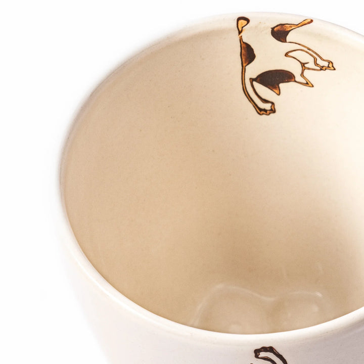 Cream-colored cup with a calico cat design reaching for a butterfly, decorated with dotted lines and paw prints.