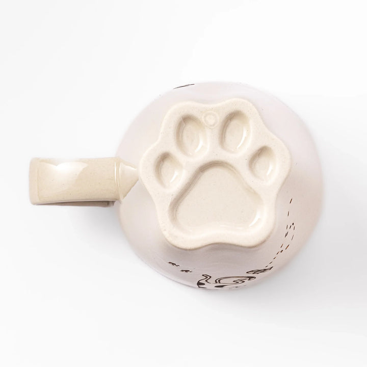 Cream-colored cup with a calico cat design reaching for a butterfly, decorated with dotted lines and paw prints.