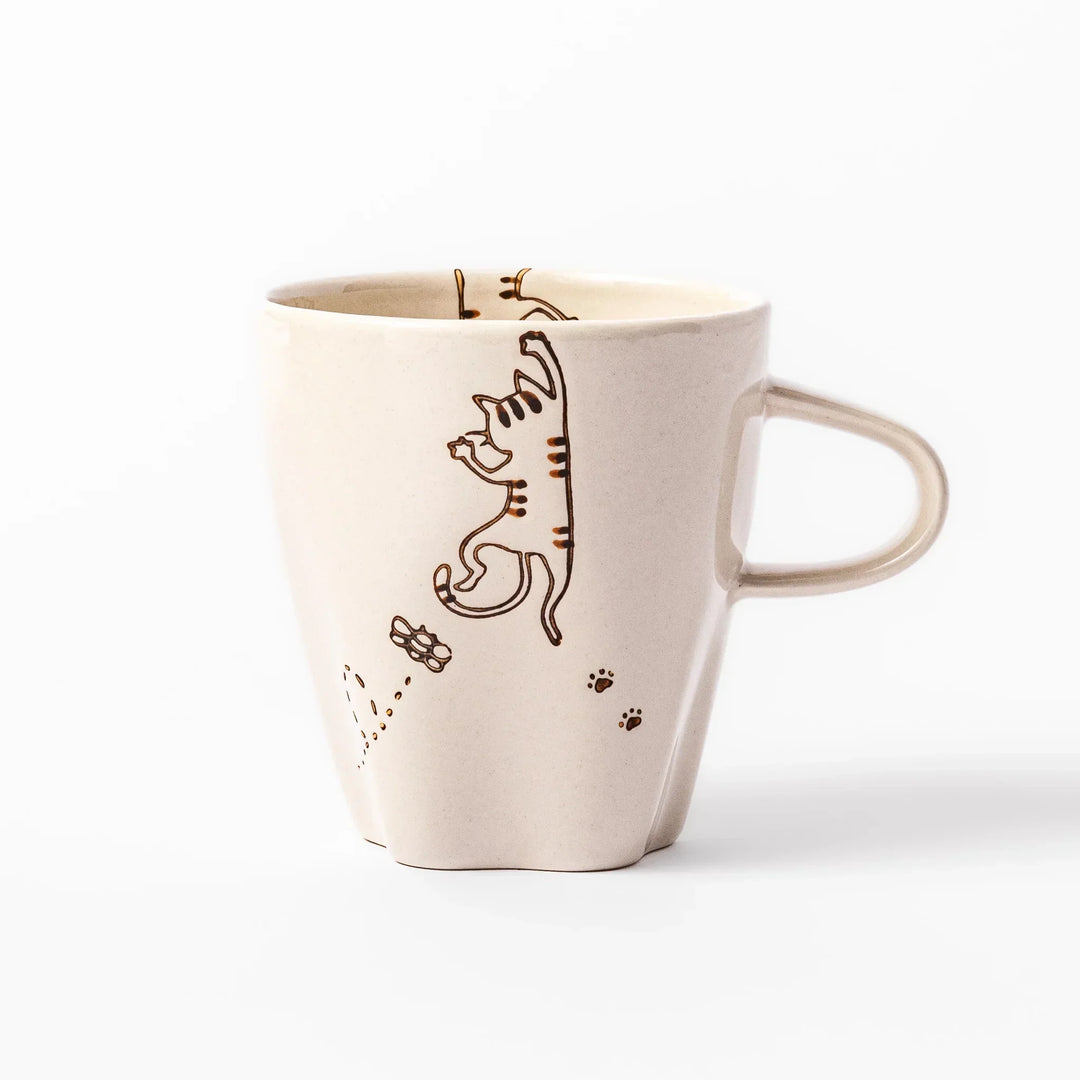 Cream-colored cup with a striped cat design reaching toward a butterfly, with dotted lines and paw prints.