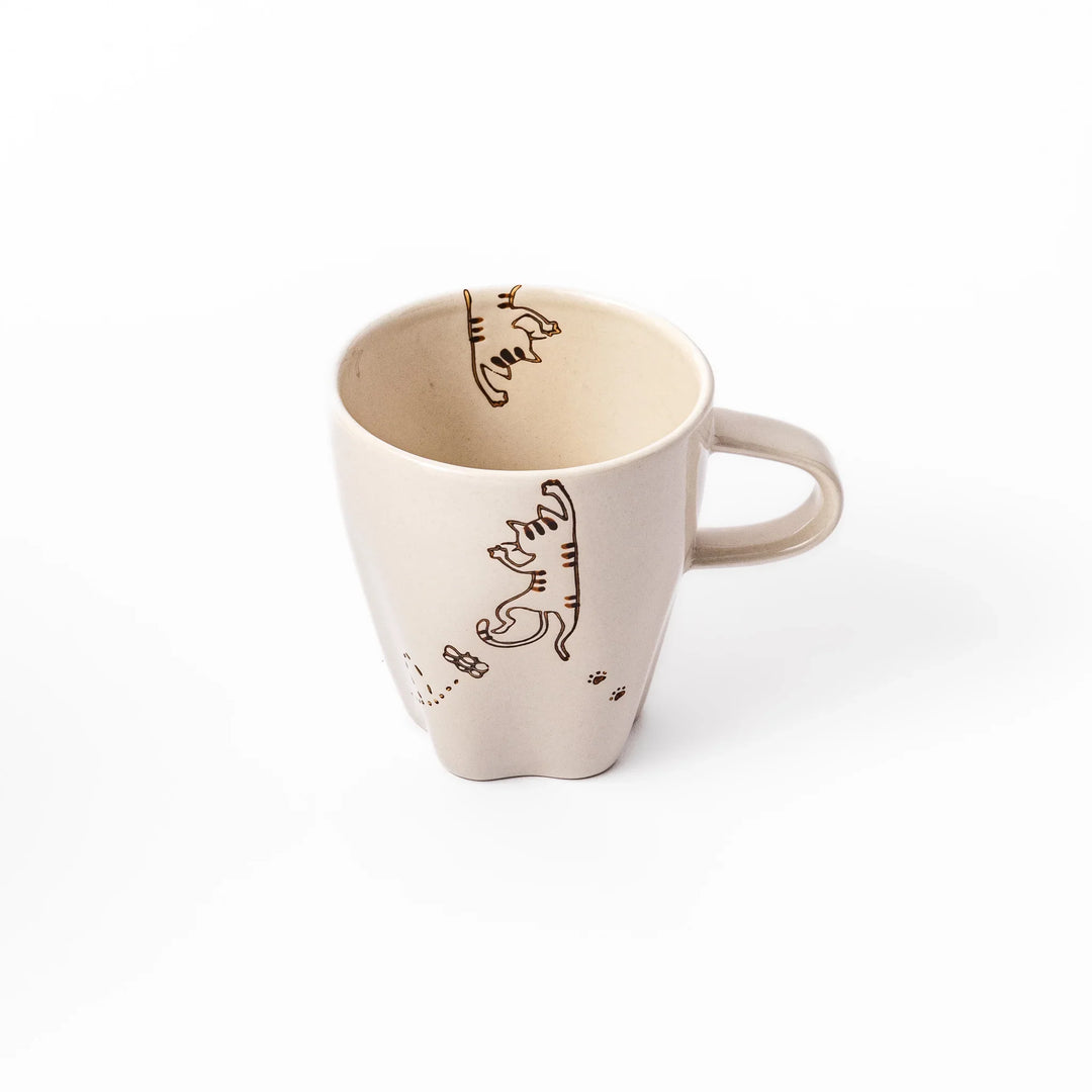 Cream-colored cup with a striped cat design reaching toward a butterfly, with dotted lines and paw prints.