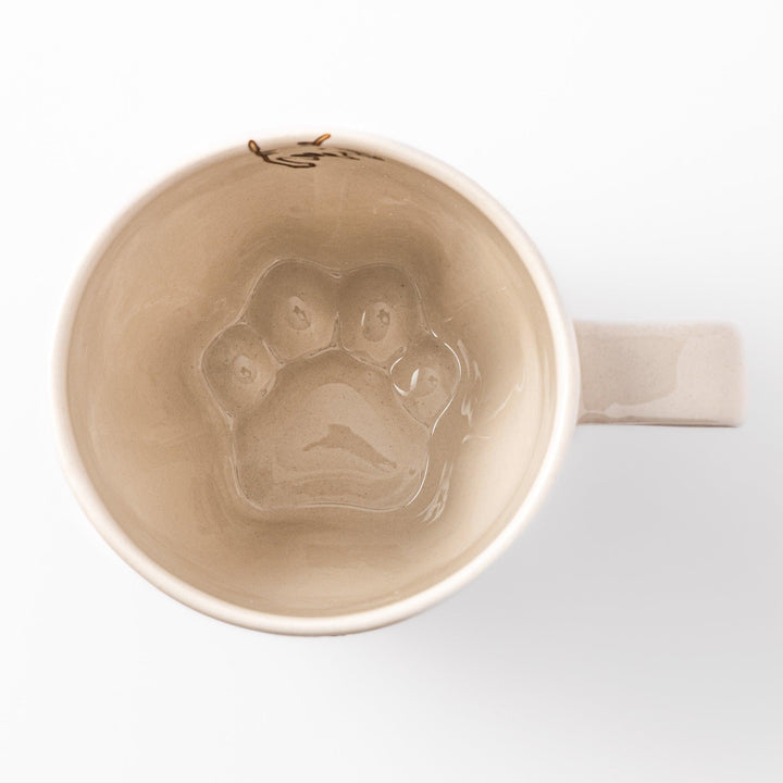 Cream-colored cup with a striped cat design reaching toward a butterfly, with dotted lines and paw prints.