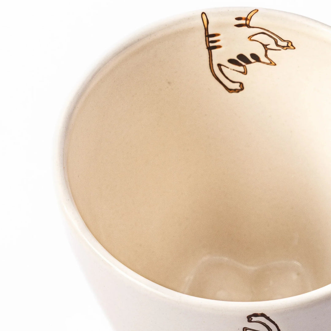 Cream-colored cup with a striped cat design reaching toward a butterfly, with dotted lines and paw prints.