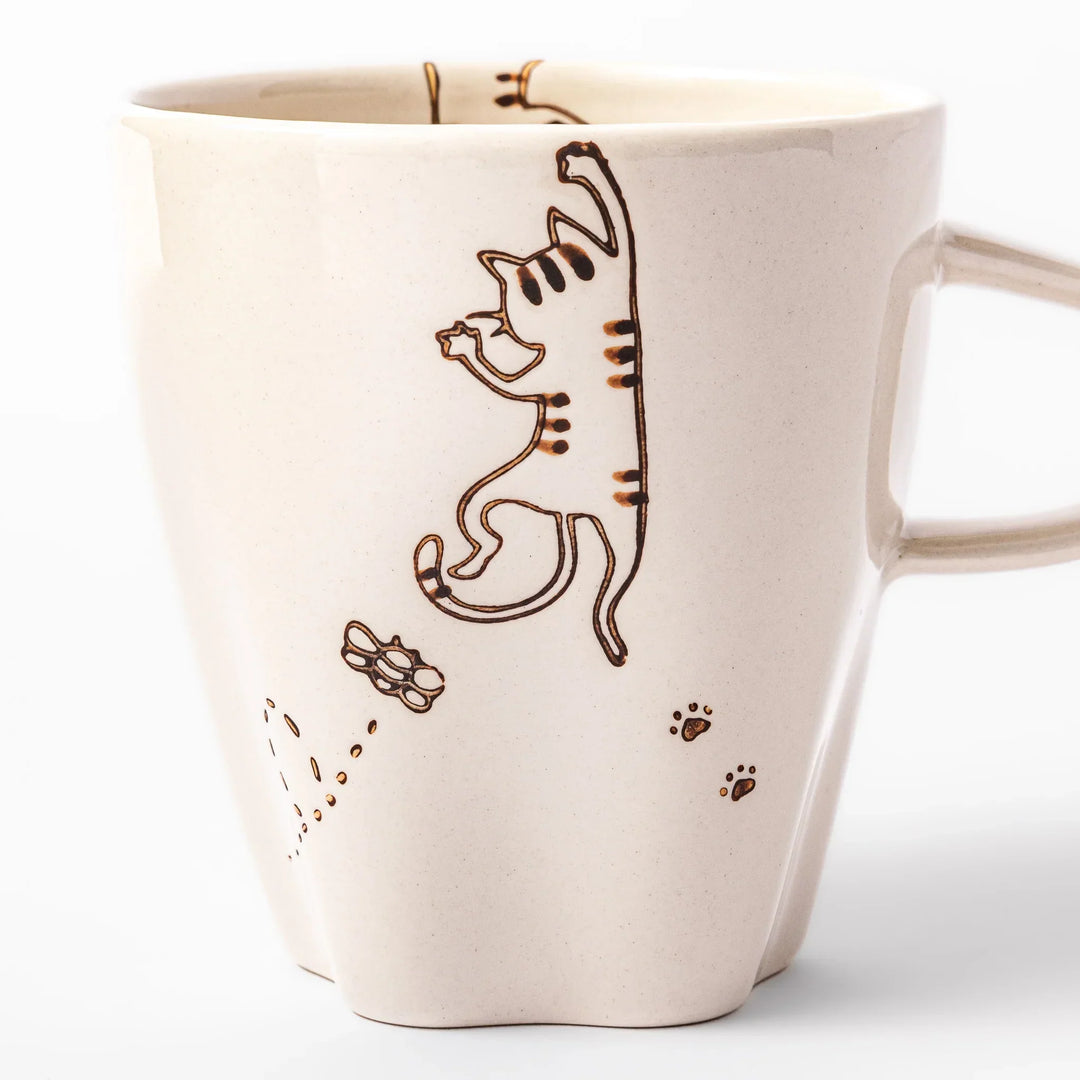 Cream-colored cup with a striped cat design reaching toward a butterfly, with dotted lines and paw prints.