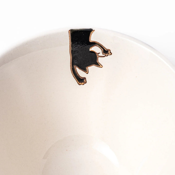 Cream-colored rice bowl with a black hanging cat, butterfly, and playful paw prints on the outside and inner rim.