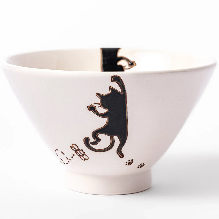 Cream-colored rice bowl with a black hanging cat, butterfly, and playful paw prints on the outside and inner rim.