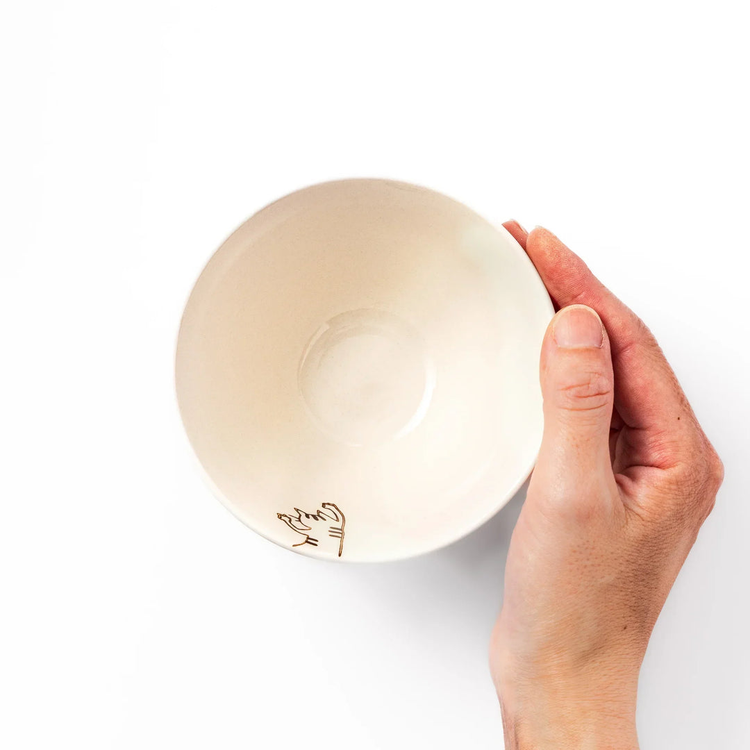 Cream-colored rice bowl with a striped hanging cat, butterfly, and dotted paw prints on the outer and inner surface.