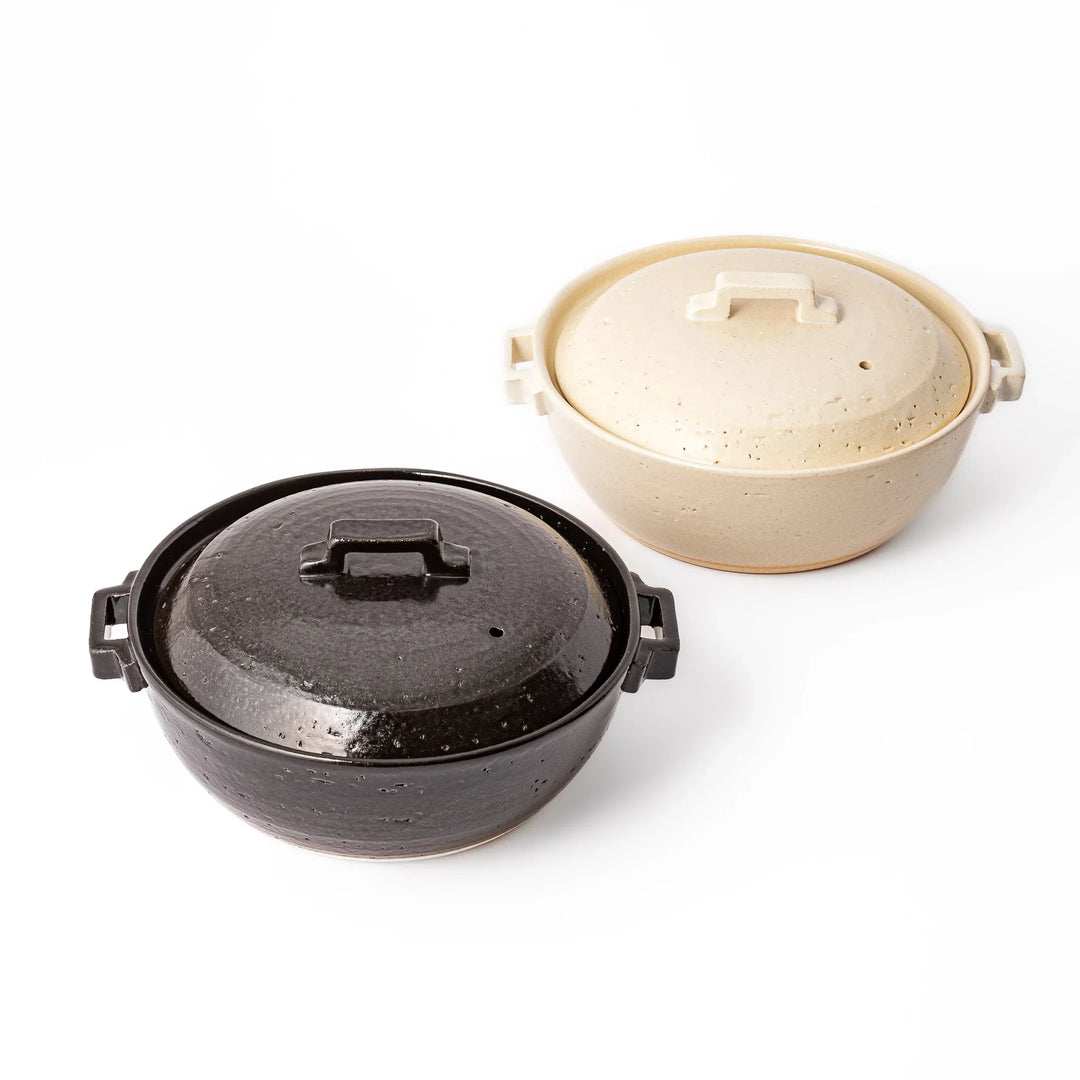 Black and white Japanese ceramic donabe pots with lids and side handles for stovetop simmering and hot pot cooking