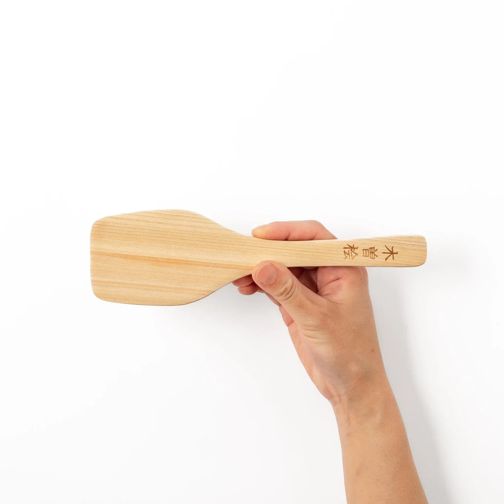 Compact hinoki wood spatula with flat angled edge and engraved handle for straining flipping and serving.