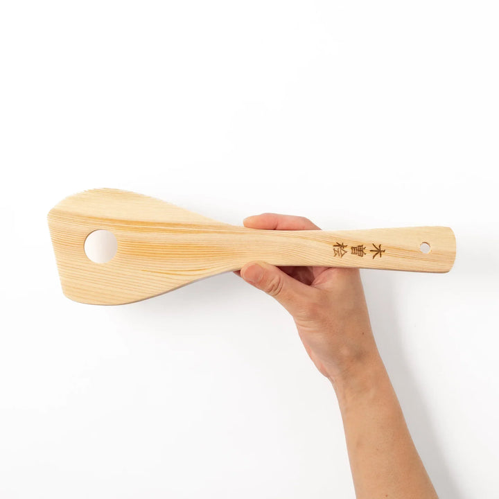 Hinoki wood slotted spatula with circular cutout and engraved handle for stirring and draining food.