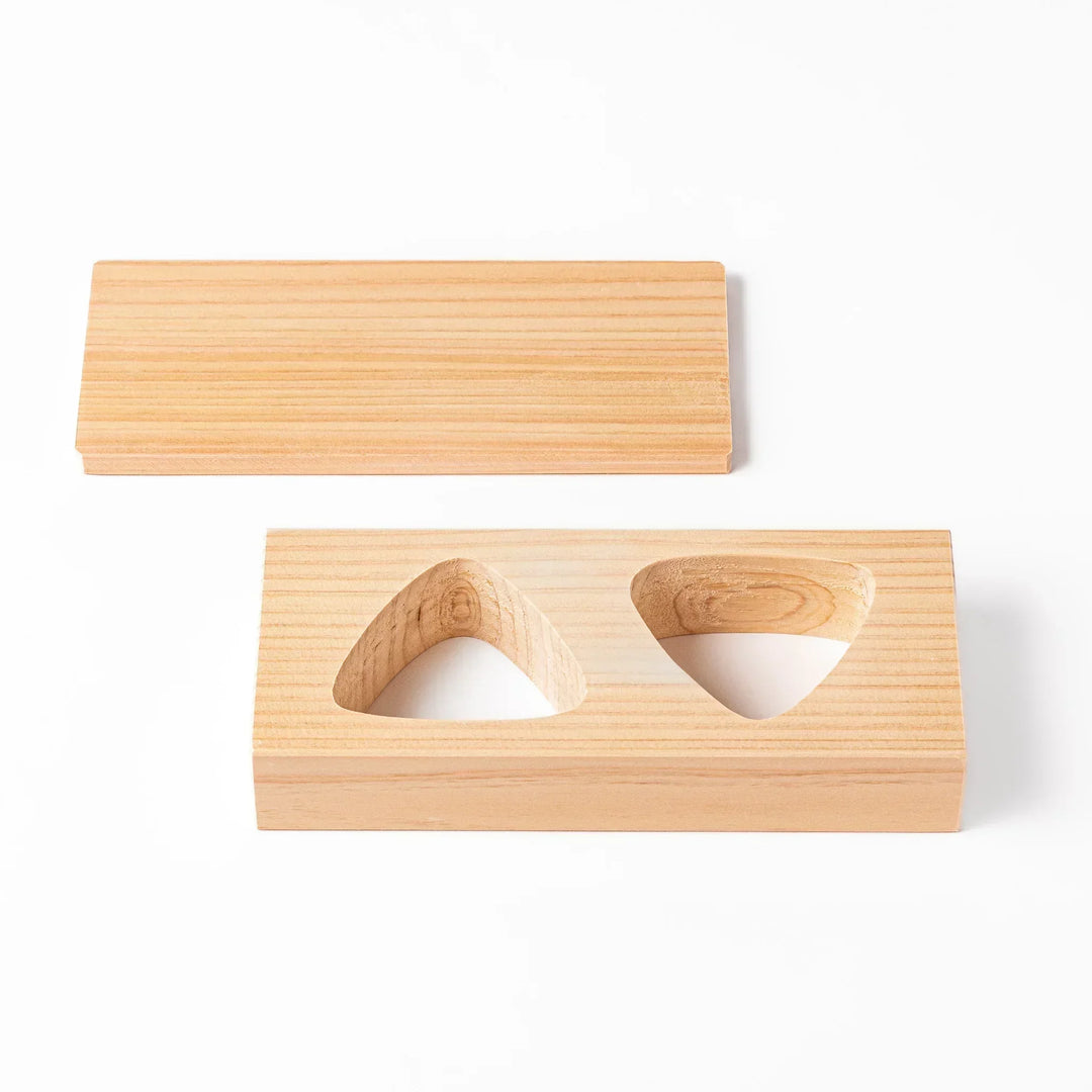 Hinoki wood onigiri mold with two triangle cavities and lid for shaping aromatic Japanese rice balls.