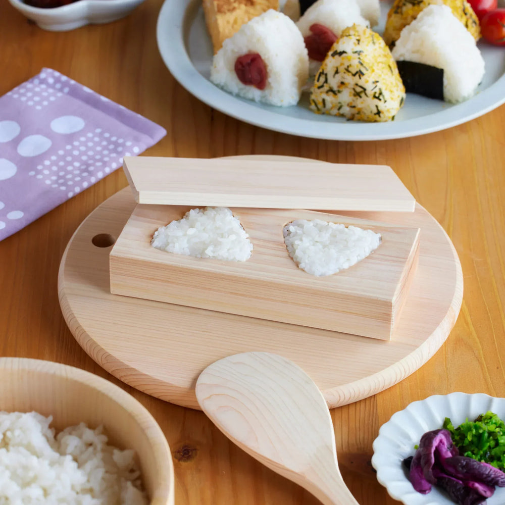 Hinoki wood double triangle onigiri mold for shaping Japanese rice balls shown with fresh rice and homemade onigiri