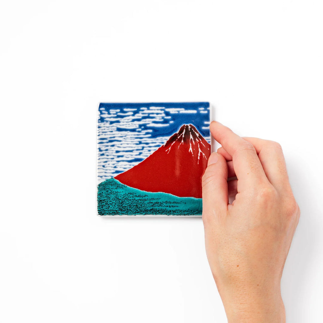 Square Japanese ceramic coaster with Hokusai Red Fuji design showing red mountain blue sky and white clouds.