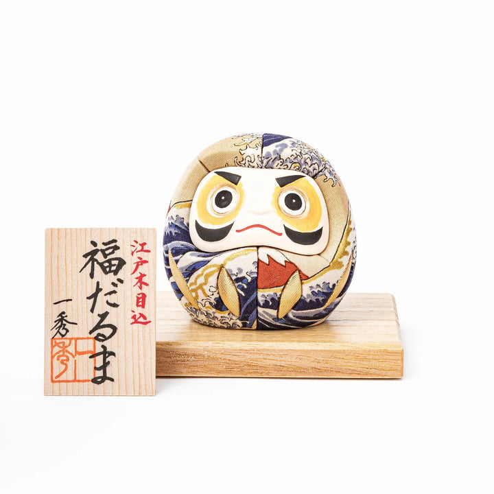 Fabric daruma ornament with bold Kabuki style face and wave pattern set on a small wooden display stand