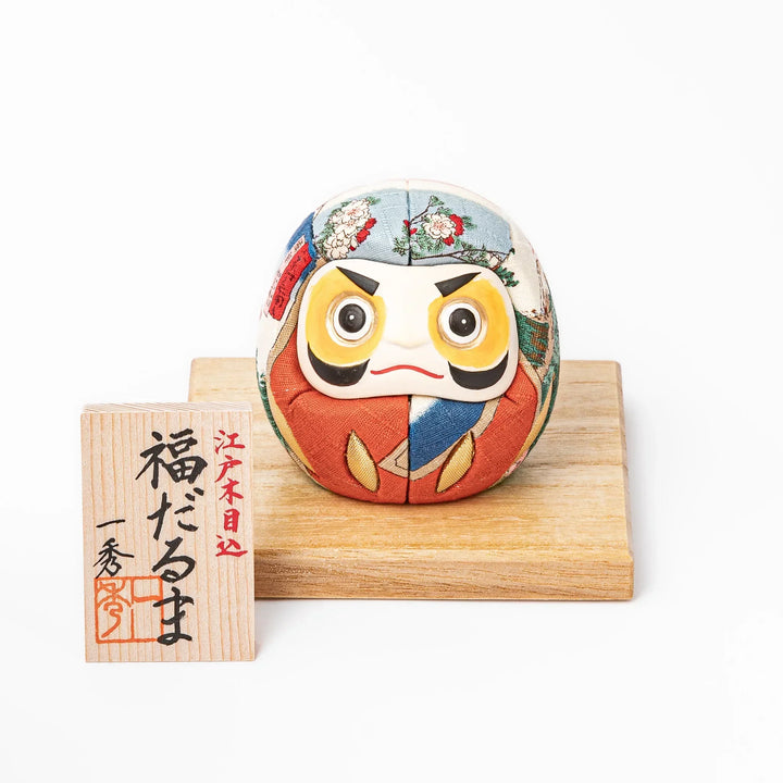 Fabric daruma ornament with bright multicolor kimono pattern and bold painted face displayed on a wooden stand