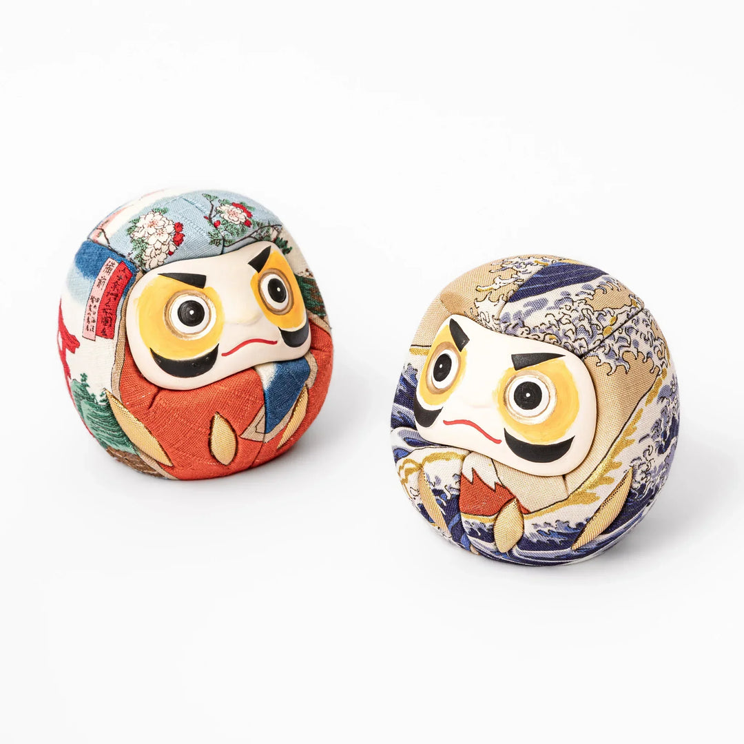 Two fabric daruma ornaments with multicolor kimono patterns displayed on wooden stands side by side